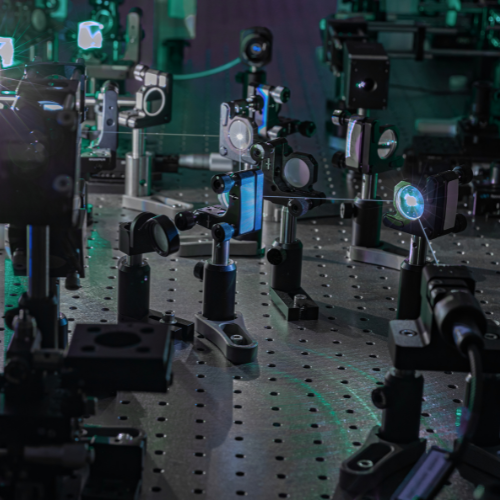 Close-up of a precision optics laboratory featuring lenses, mirrors and optical components mounted on an experimental table. Beams of light pass through the equipment, representing photonics research, optical engineering, laser technology and advanced scientific innovation.